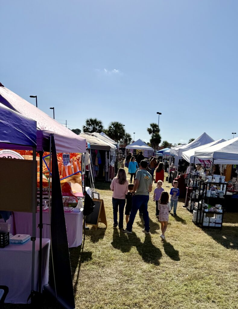 vendors set up in a row with shoppers walking down the row at an event at The Fort Container Park